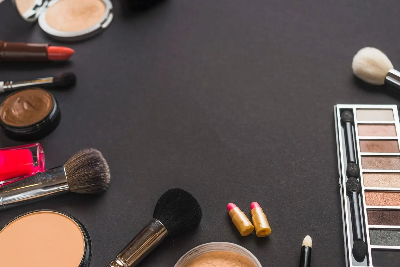Overhead view of makeup brushes and cosmetic products on a black background